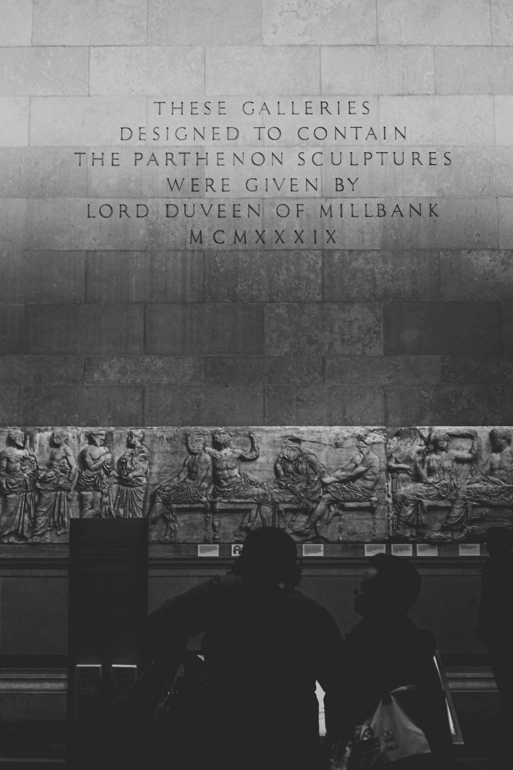 grayscale photo of man in black jacket standing in front of wall with graffiti