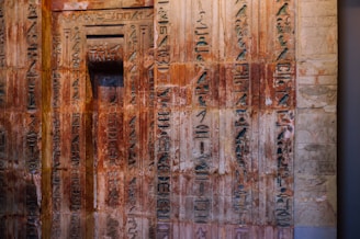 Ancient wall covered with intricate hieroglyphs, some areas showing signs of wear and aging. The engravings display a variety of symbols and characters, indicating a historical or cultural significance.