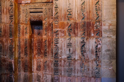 Ancient wall covered with intricate hieroglyphs, some areas showing signs of wear and aging. The engravings display a variety of symbols and characters, indicating a historical or cultural significance.