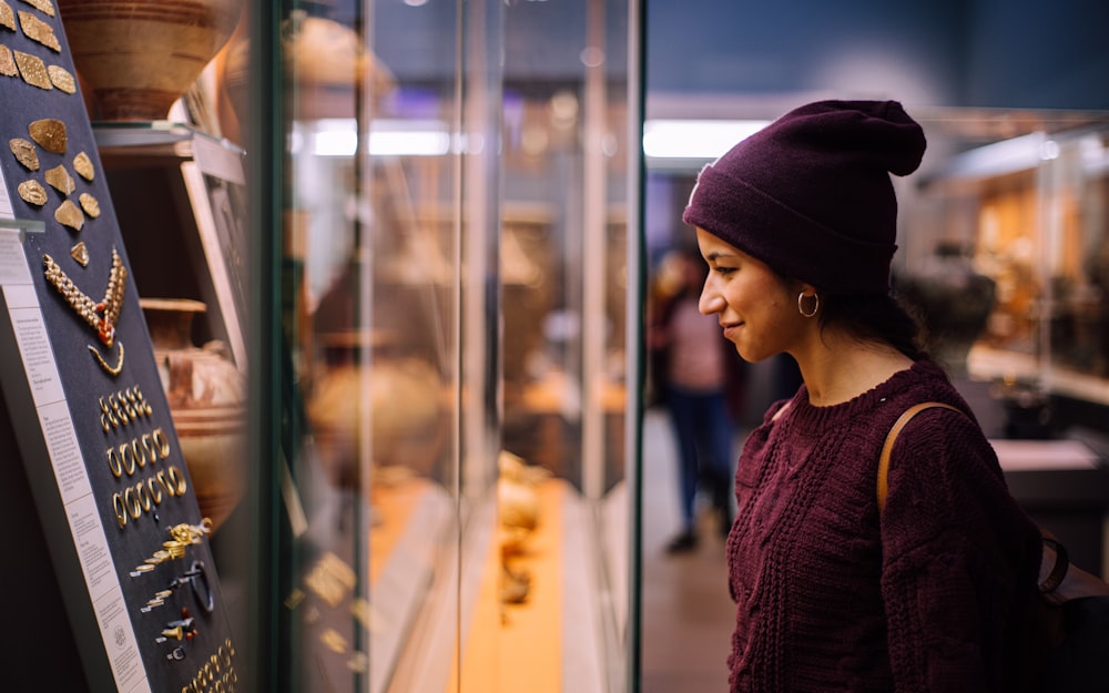 Mujer con gorro de punto púrpura y suéter de punto púrpura mirando la ventana de vidrio