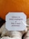 A close-up of a white tag with maroon-colored text that reads 'Schmerz ist immer vergänglich. Pain is never permanent.' The tag is attached to a string and placed against a background of ginger root and an orange.