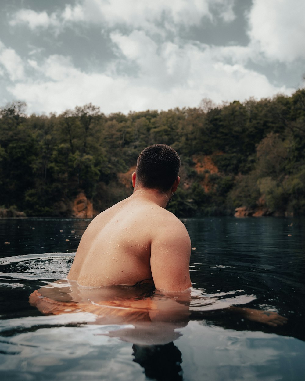 topless man in water near green trees during daytime