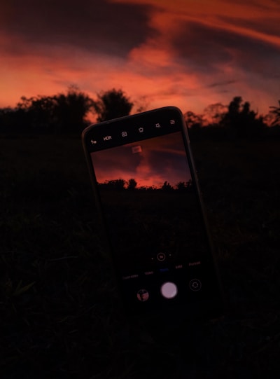 A close-up shot of a smartphone capturing a vibrant sunset over a city skyline.