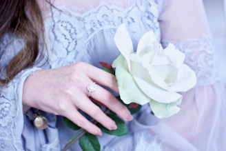 Elegant woman in regal attire holding a delicate rose, framed by soft golden light and flowing shapes.