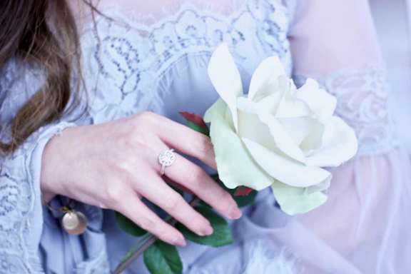 Elegant woman in regal attire holding a delicate rose, framed by soft golden light and flowing shapes.