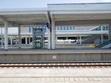 A modern train station platform with multiple tracks and an accessible elevator. The platform is clean and well-structured with overhead roofing. A high-speed train labeled CRH is partially visible in the background. There are also ramps and stairs leading to elevated sections.