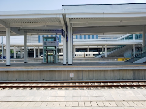 A modern train station platform with multiple tracks and an accessible elevator. The platform is clean and well-structured with overhead roofing. A high-speed train labeled CRH is partially visible in the background. There are also ramps and stairs leading to elevated sections.