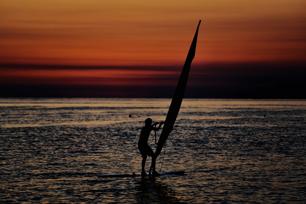 silhouette of woman standing on sea shore during sunset