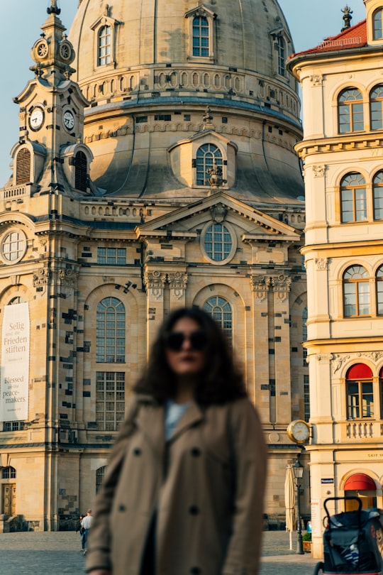 woman in gray coat standing near blue and white concrete building during daytime in Frauenkirche Dresden Germany