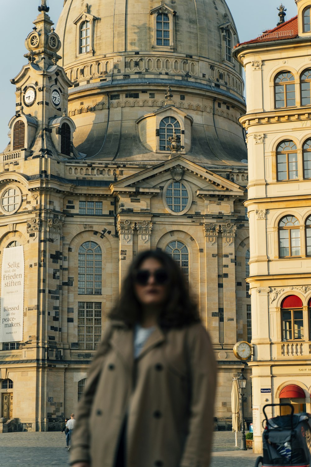 woman in gray coat standing near blue and white concrete building during daytime