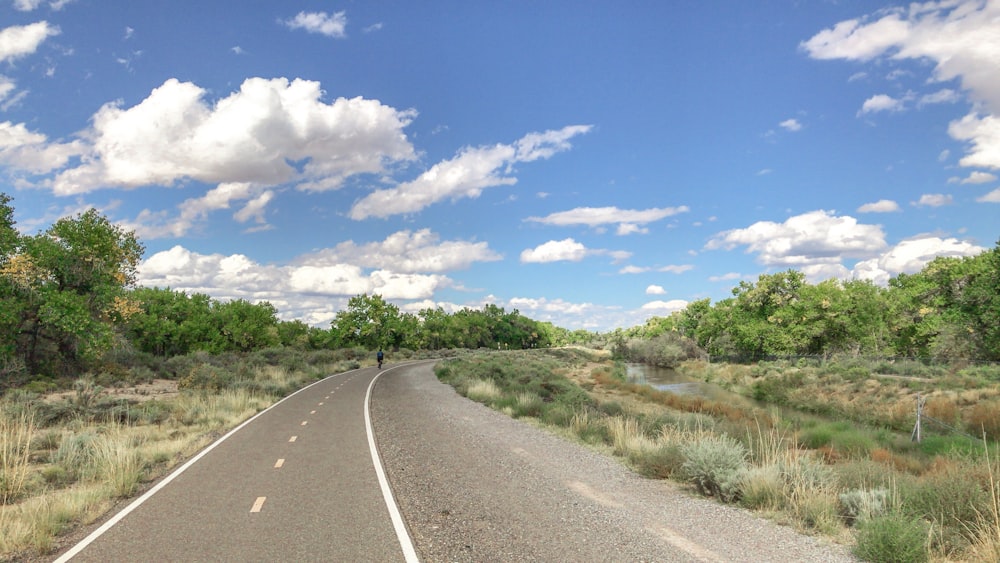 gray concrete road between green grass field under blue and white cloudy sky during daytime