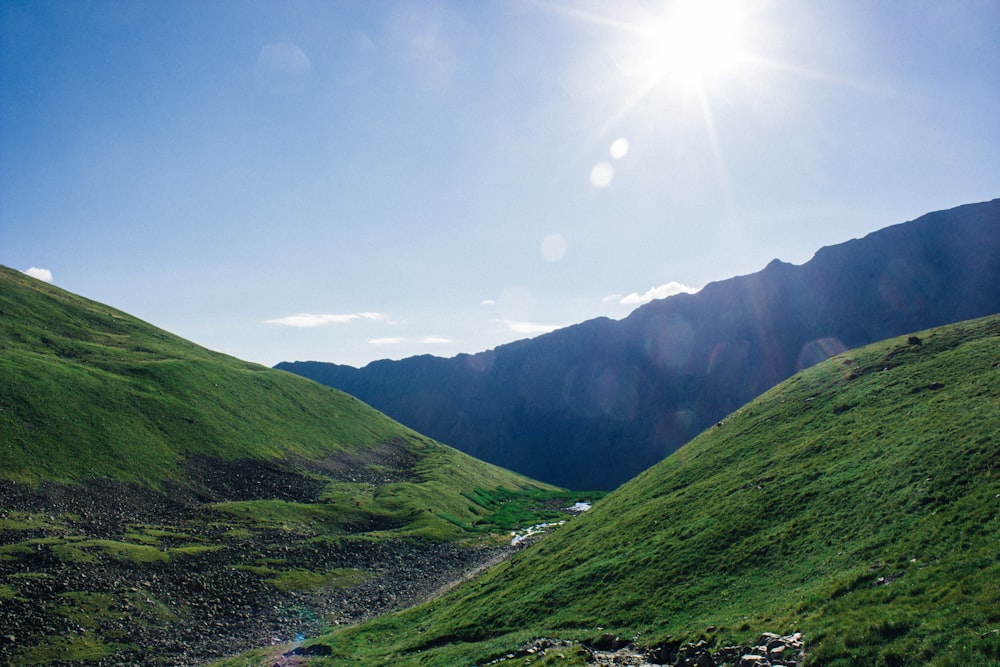 green grass field and mountains under blue sky during daytime