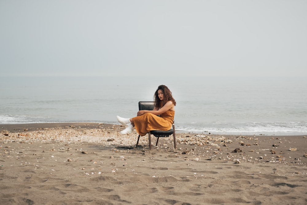 woman in brown jacket and white pants sitting on brown wooden chair on beach during daytime