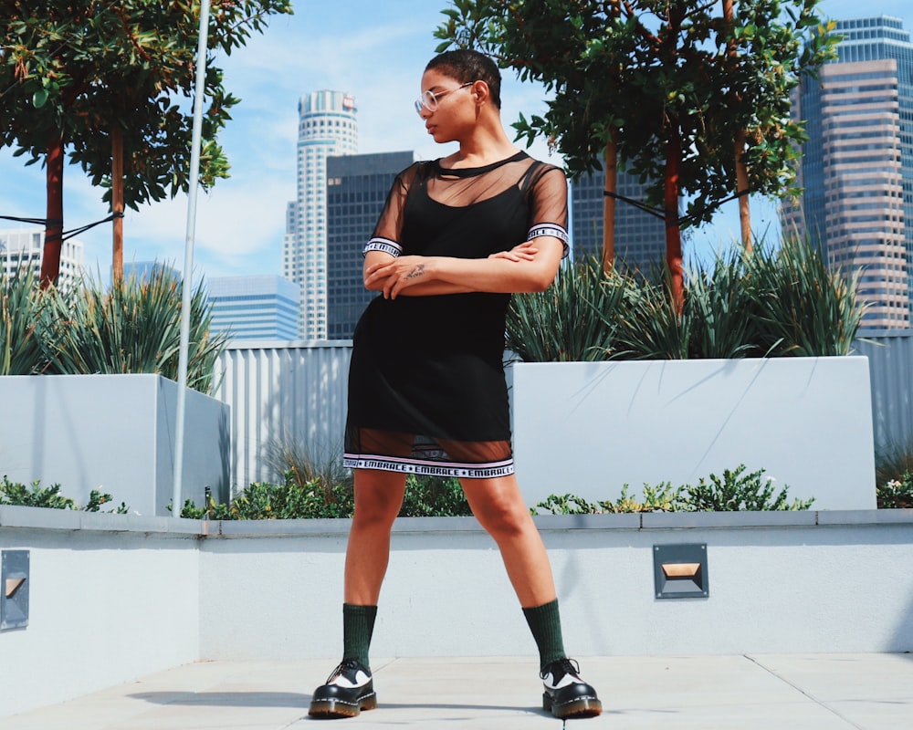 Frau in schwarzem ärmellosem Kleid und schwarzen Nike-Laufschuhen auf grauem Betonboden während