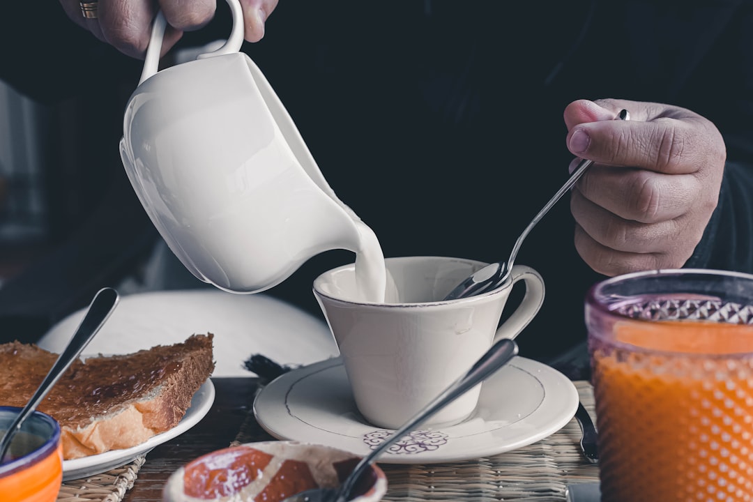 person pouring white liquid on white ceramic mug