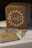A cardboard box labeled 'Cards' is placed on a table. The box is decorated with a white floral wreath design. Surrounding the box are scattered pages from books and a guest book, which is closed and sits nearby.