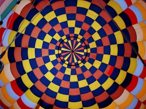 A vibrant and symmetric pattern of concentric circles composed of alternating blue, yellow, orange, and red squares. The design is reminiscent of a kaleidoscope, with lines radiating from the center creating a sense of depth.