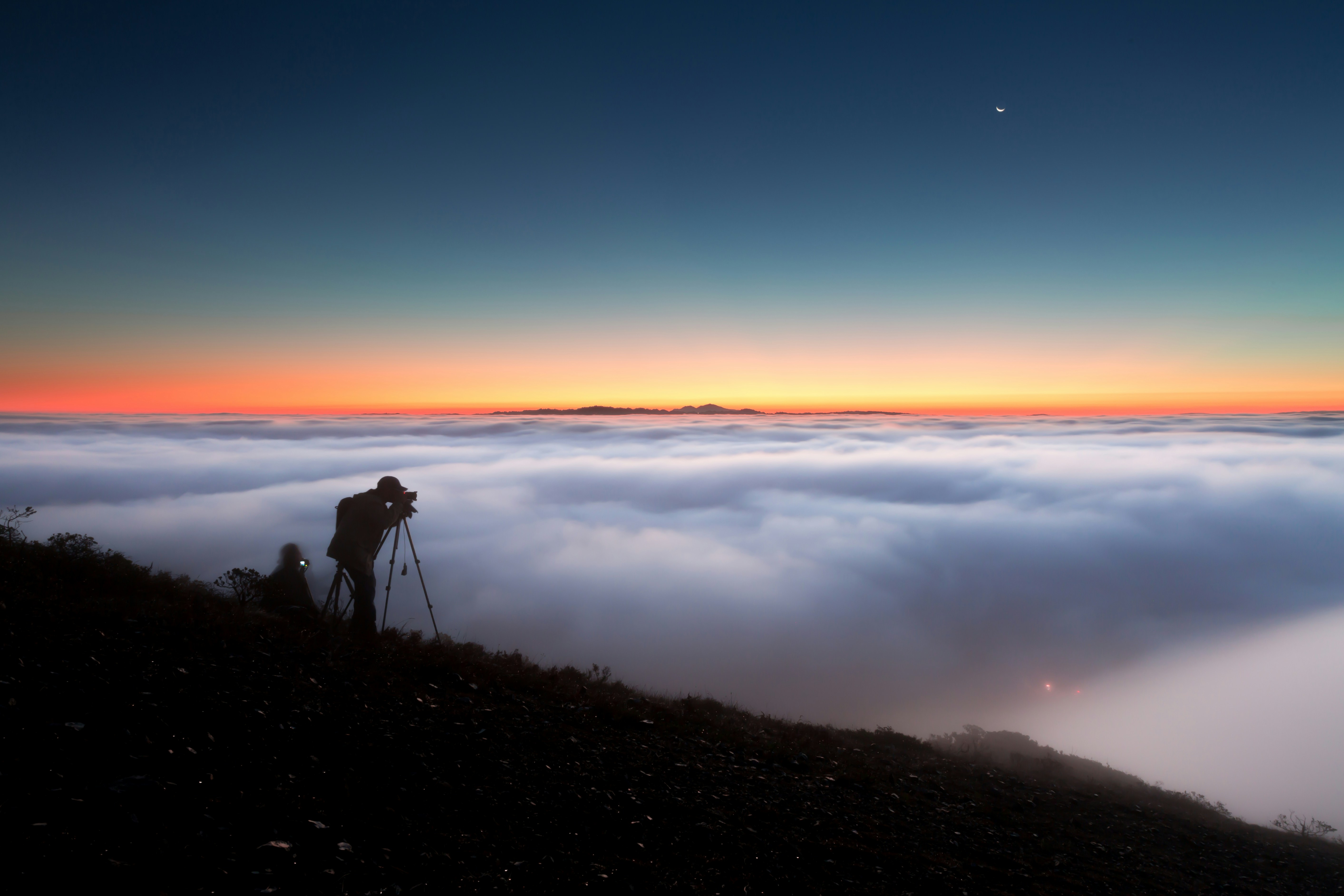 silhouette of person standing on rock near body of water during sunset