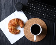Close-up of a delicate croissant on a rustic wooden table beside an open journal and fountain pen.