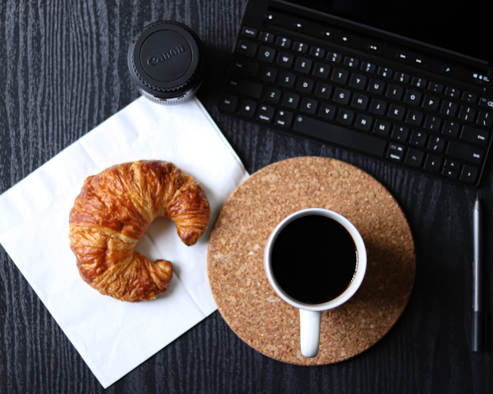 doughnut on white ceramic plate beside black ceramic mug