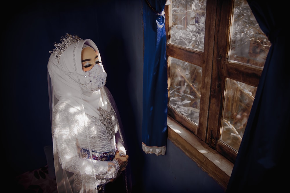 woman in white hijab standing beside blue curtain