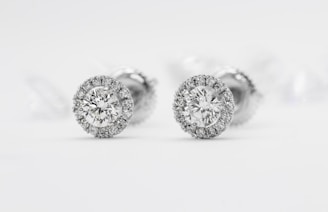Elegant diamond stud earrings with a halo setting surrounded by smaller diamonds on a reflective white surface.