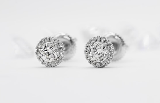 Elegant diamond stud earrings with a halo setting surrounded by smaller diamonds on a reflective white surface.
