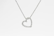 A heart-shaped pendant encrusted with small diamonds is suspended from a delicate chain. The chain appears to be made of tiny, round metal beads, and the pendant sparkles against a white background.