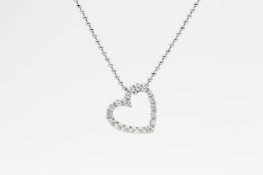 A heart-shaped pendant encrusted with small diamonds is suspended from a delicate chain. The chain appears to be made of tiny, round metal beads, and the pendant sparkles against a white background.