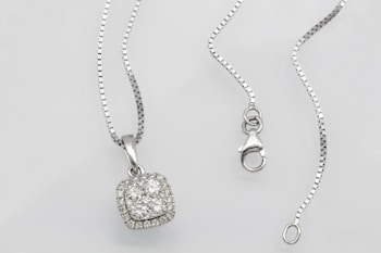 A silver necklace with a square pendant encrusted with multiple small diamonds is laid out on a flat surface. The chain is delicate and features a lobster clasp closure. The overall look is elegant and sophisticated.