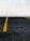 A section of a parking lot with yellow lines on the asphalt indicating parking spaces. The background consists of a wall covered in white tiles arranged in a grid pattern.