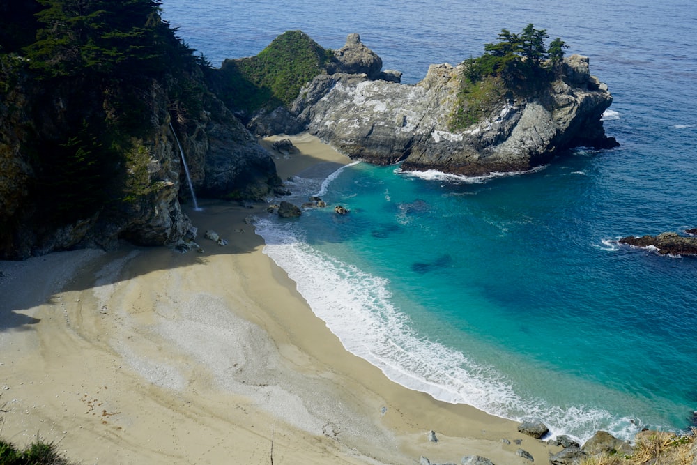 a sandy beach next to the ocean near a cliff