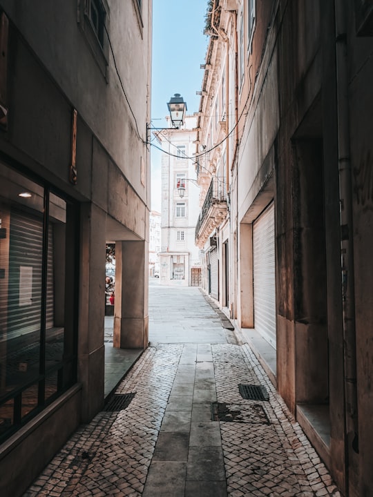 brown brick pathway between brown brick buildings during daytime in Coimbra Portugal