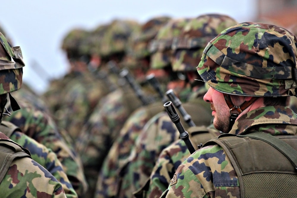 homem no uniforme de camuflagem verde e marrom segurando rifle preto