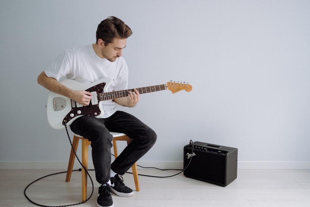 uomo in t-shirt girocollo bianca che suona la chitarra elettrica