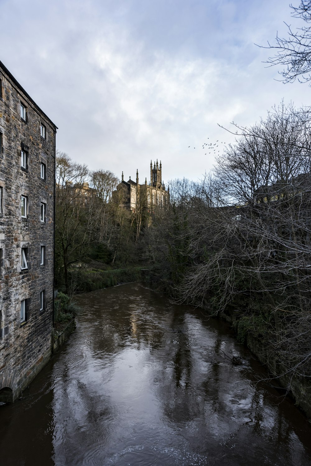 brown brick building beside river under cloudy sky during daytime