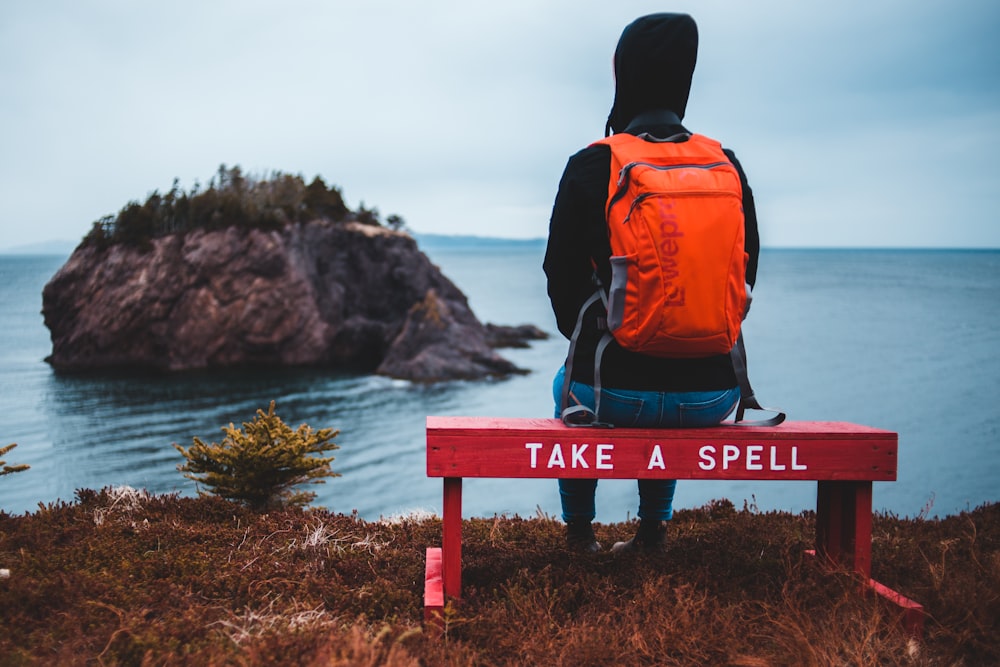 man in orange and black backpack sitting on blue wooden bench