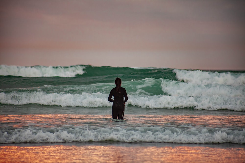 man in black wetsuit standing on sea shore during daytime