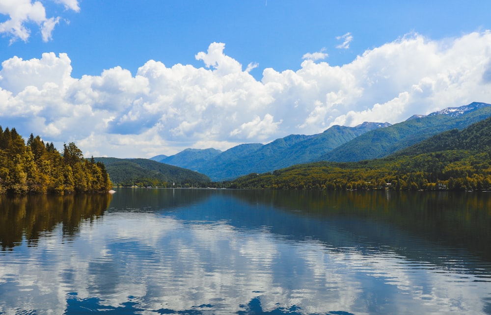 green trees and mountain beside lake under blue sky and white clouds during daytime