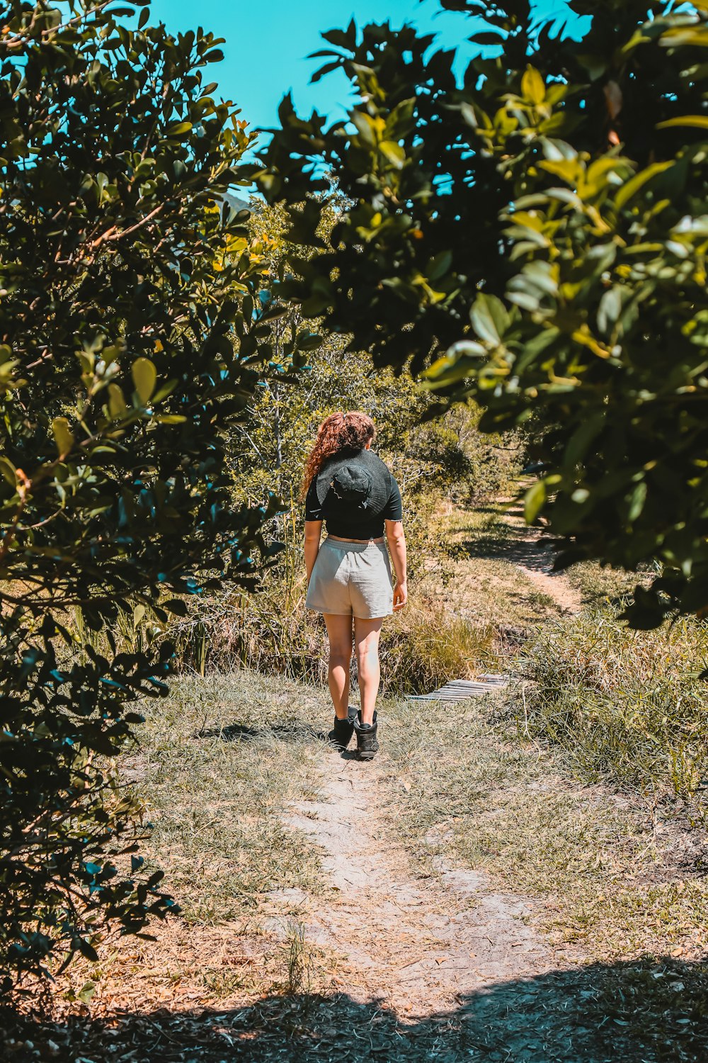woman in black t-shirt walking on dirt pathway between green plants during daytime