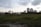 A landscape with a foreground of green grass and a backdrop of high-rise buildings under a cloudy sky.