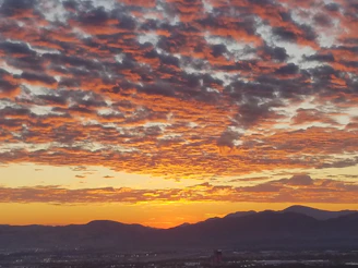 A vibrant sunset over a mountain range with a lone traveler taking photos.