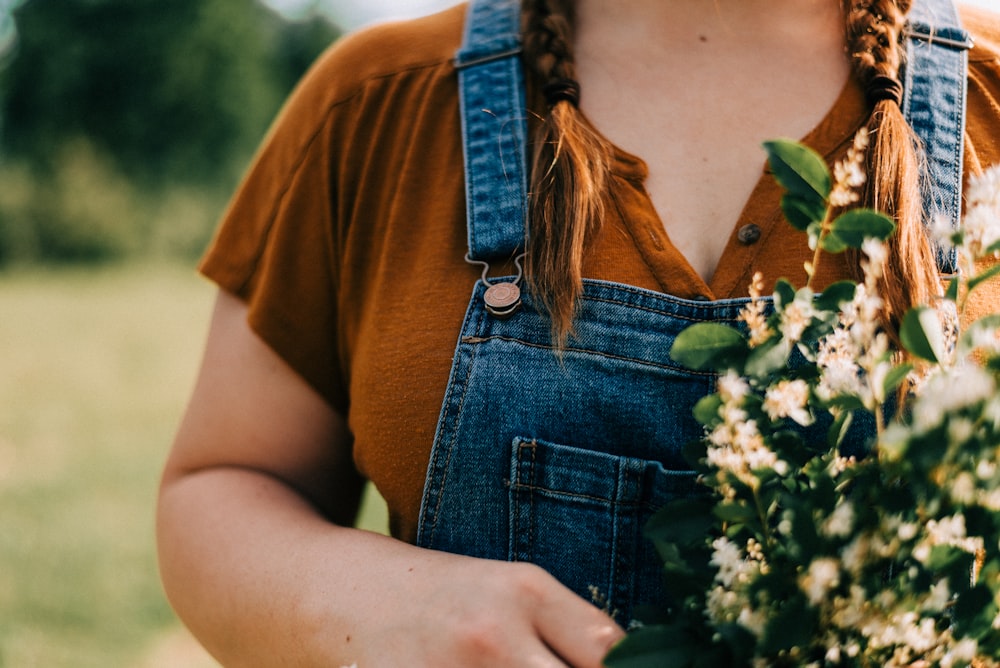 Frau in braunem Rundhals-T-Shirt und blauer Jeanslatzhose mit weißen Blumen