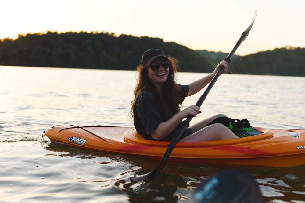 Frau im schwarzen Hemd fährt tagsüber mit orangefarbenem Kajak auf dem See