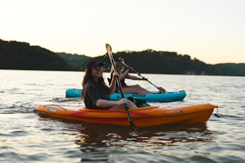 woman in blue shirt and blue denim jeans riding orange kayak on water during daytime