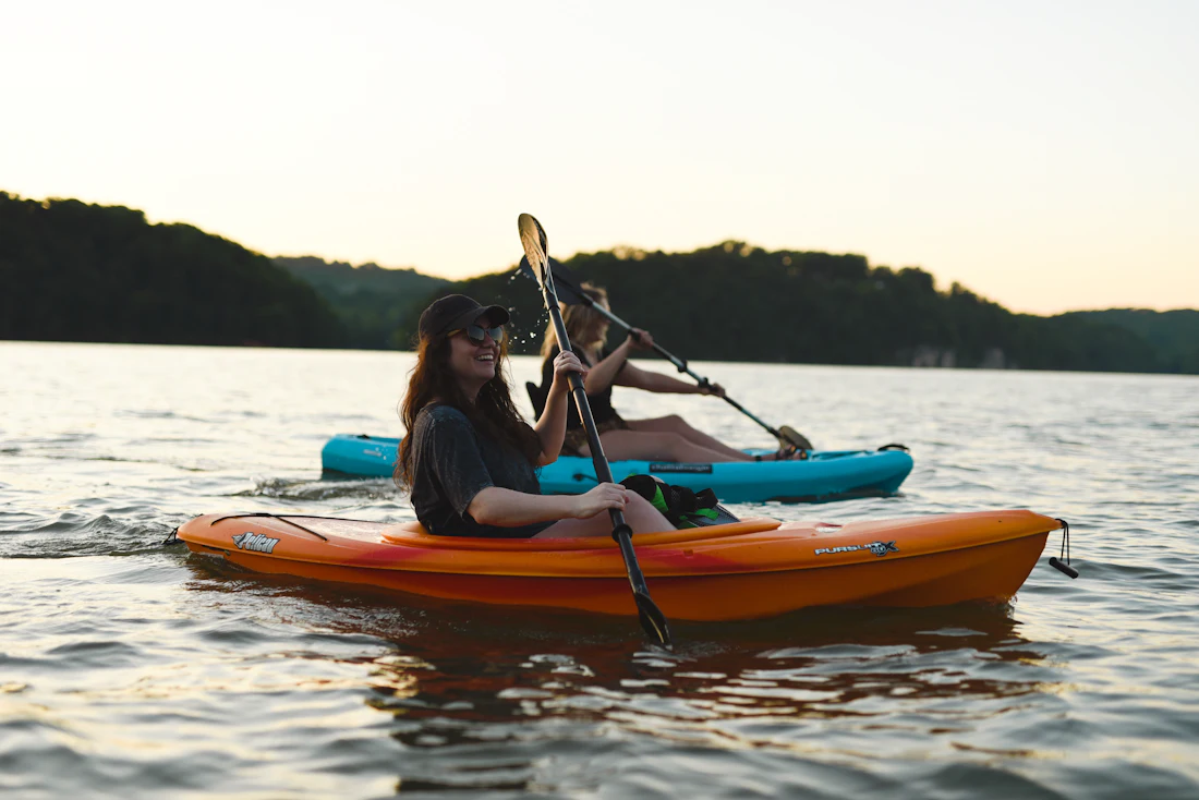 A camper paddling an orange kayak across calm lake water
