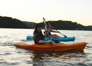 woman in blue shirt and blue denim jeans riding orange kayak on water during daytime