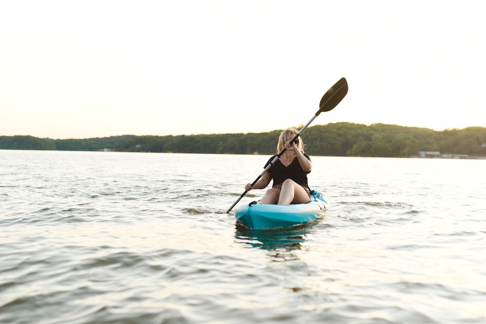 woman in blue bikini sitting on blue kayak on body of water during daytime