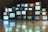 A collection of vintage television sets are stacked upon each other, each displaying static or random color bandwidth. These TVs create an artistic installation with reflections visible on the polished floor, presenting a nostalgic and retro aesthetic.
