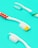 Three toothbrushes are placed on a bright turquoise background. The toothbrushes have white handles with different colored accents. One has red polka dots, another has blue and green stripes, and the last one has a simple cyan accent. The bristles of the brushes are white with some yellow and cyan highlights.